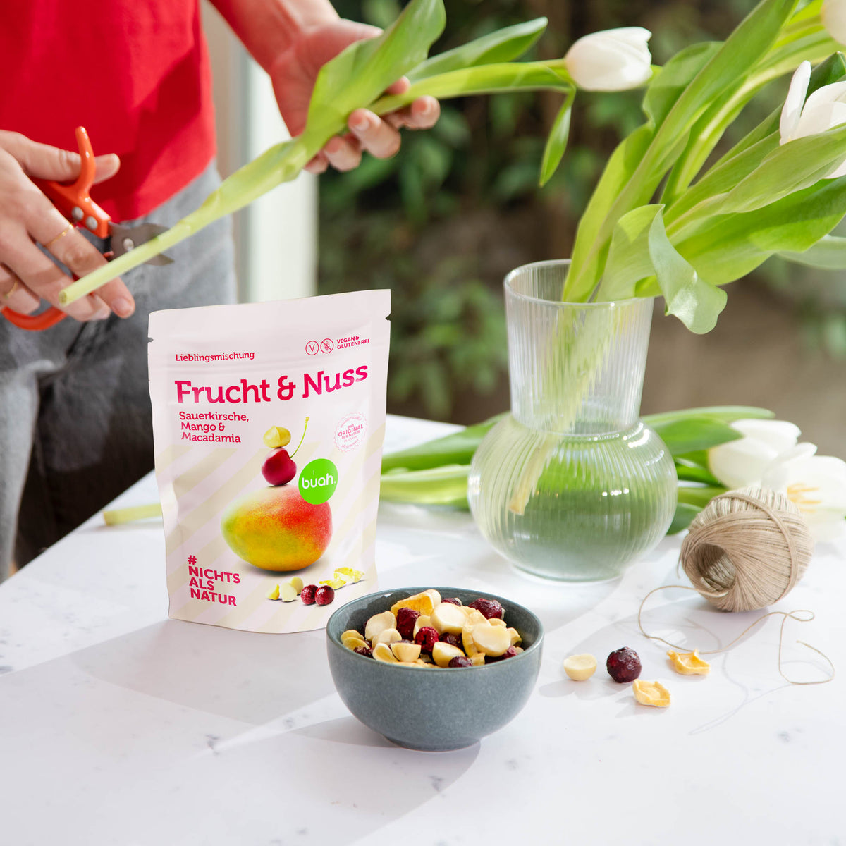 buah Frucht & Nuss Mischung mit Macadamia auf einem Tisch neben einer Vase mit weissen Tulpen