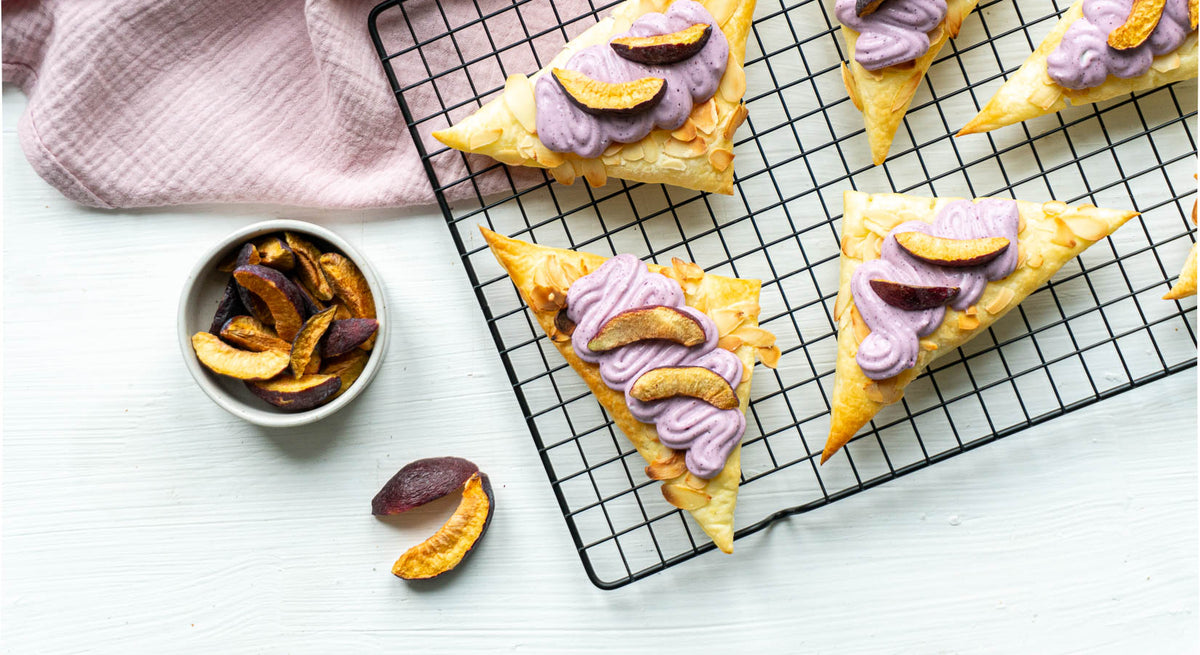 Blätterteig Schnecken mit Topping aus lila Joghurt und buah gefriergetrockneten Pflaumen liegen auf Backgitter, daneben buah Pflaume in einer Schale