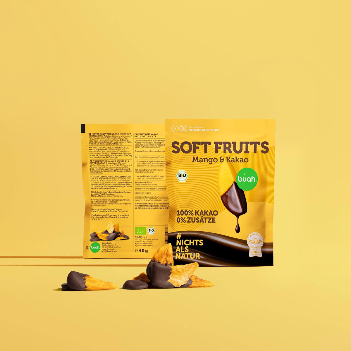 buah Soft Fruits Mango & Kakao, 40 g: Beutel mit dem Hinweis „100% Kakao, 0% Zusätze“, davor getrocknete Mangoscheiben, zur Hälfte mit dunklem Kakaoüberzug. Dahinter ein Beutel mit Rückseite.